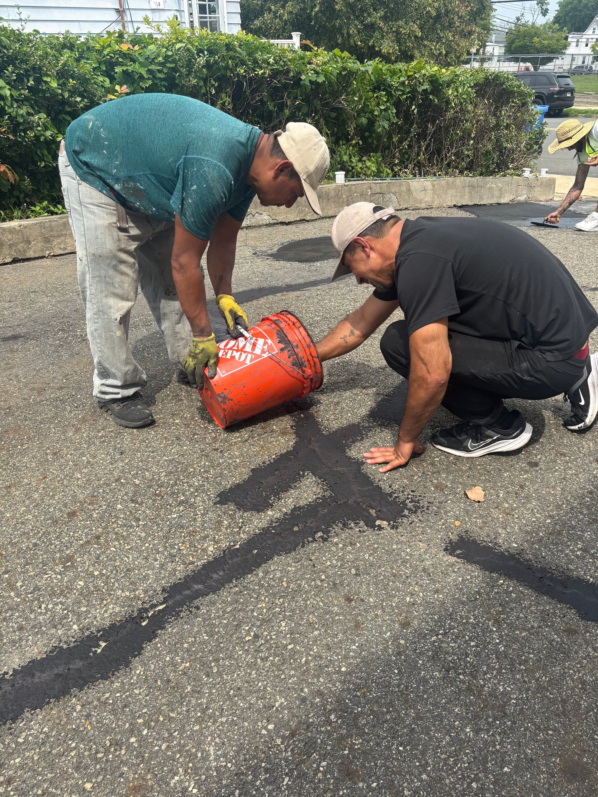 Crew pouring hot sealant along a crack line in the driveway